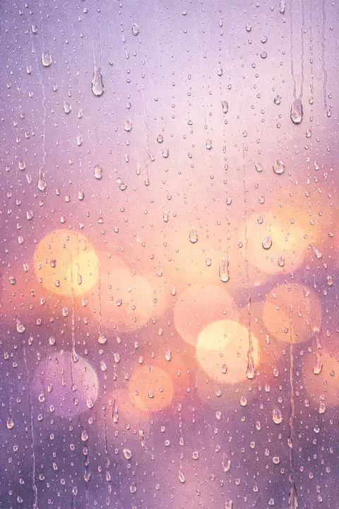 Aesthetic rain wallpaper with soft rain beads on a window and warm blurred bokeh behind