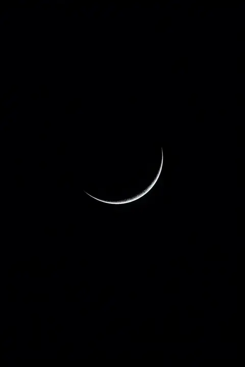 Black wallpaper of a thin silver crescent moon on true black