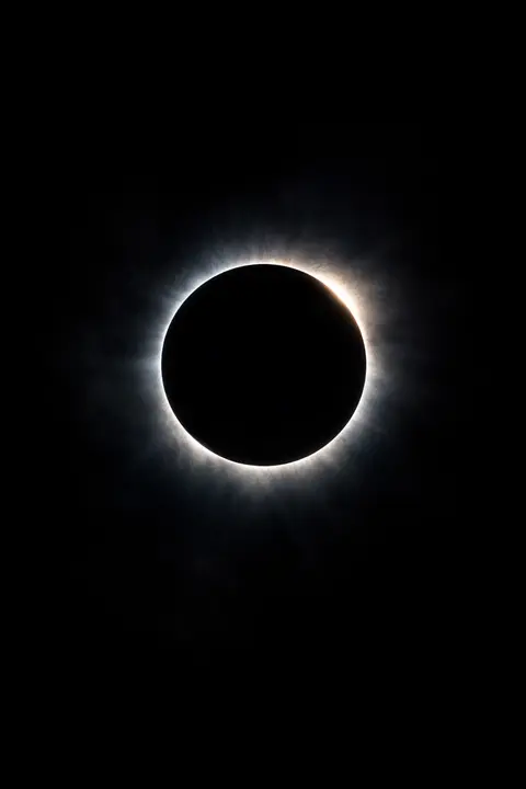 Dark wallpaper with a total eclipse, a black disc ringed by a thin bright corona of light