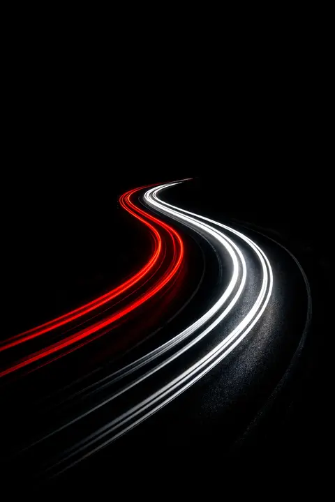 Dark wallpaper with long red and white vehicle light trails sweeping along a night road