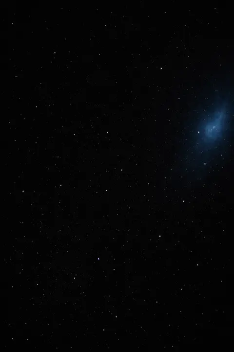 Black space wallpaper with a near black sky, small sharp white stars and one faint blue glow