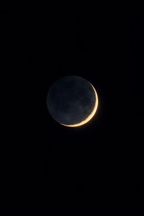 Black space wallpaper with a thin crescent moon and faint earthshine on an empty black sky