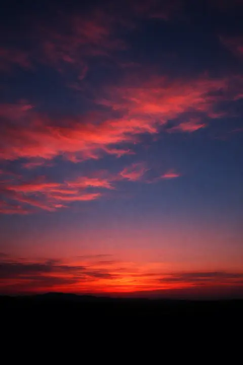 Sunset wallpaper with afterglow clouds lit salmon and rose above completely dark land