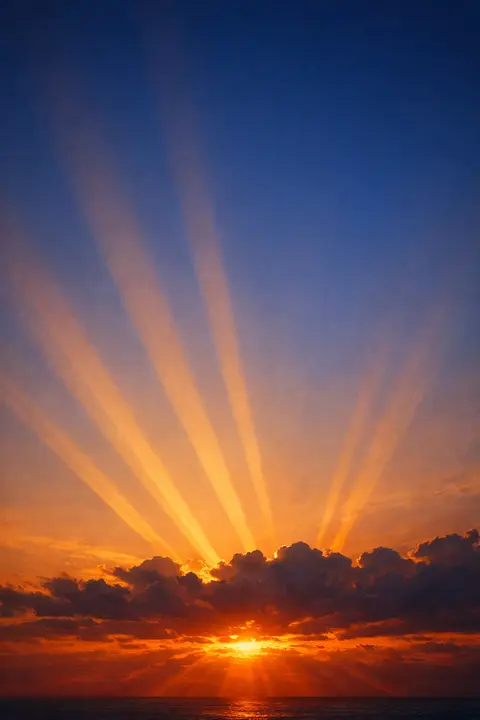 Sunset wallpaper with golden crepuscular rays fanning out from behind a low cloud bank