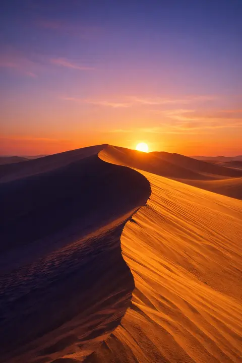 Sunset wallpaper with desert dunes in gold and shadow under a low sun on the horizon