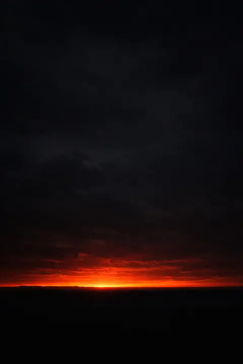 Dark sunset wallpaper with a charcoal sky, black land and one ember orange strip at the horizon