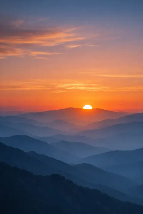 Sunset wallpaper with layered mountain ridges fading into haze under an amber setting sun